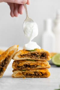 a person drizzling sour cream on a stack of quesadillas.