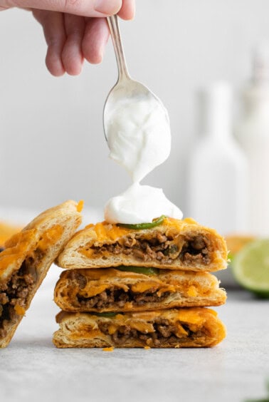 a person drizzling sour cream on a stack of quesadillas.