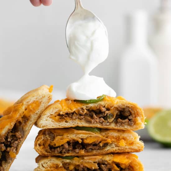 a person drizzling sour cream on a stack of quesadillas.