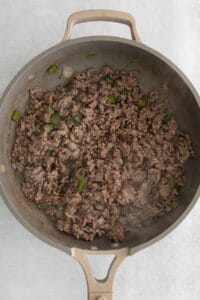 a frying pan with ground beef and green peppers.