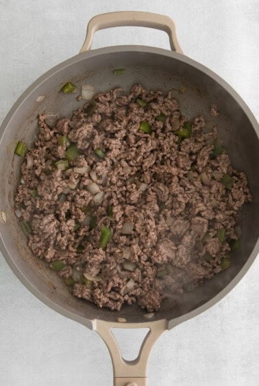 a frying pan with ground beef and green peppers.