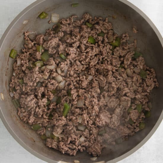a frying pan with ground beef and green peppers.