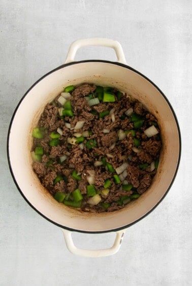ground beef in a pot with onions and green peppers.