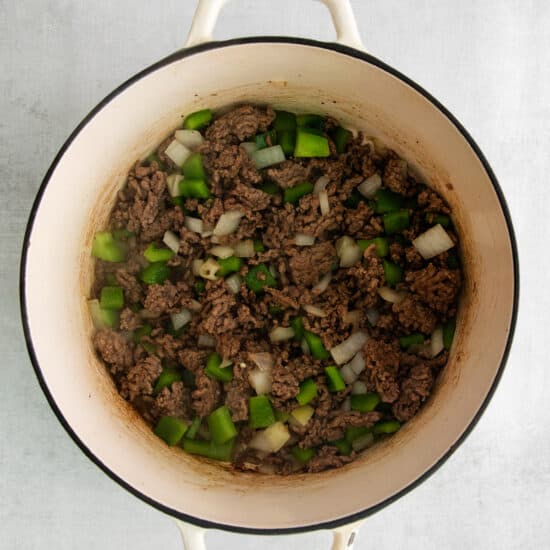 ground beef in a pot with onions and green peppers.