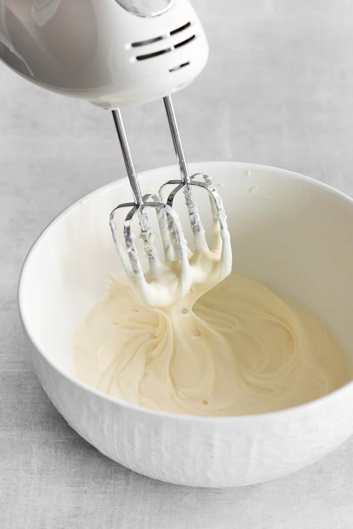 Whipped cream cheese frosting in a bowl with a hand mixer. 