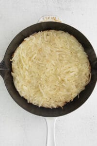 a skillet full of shredded potatoes on a white background.