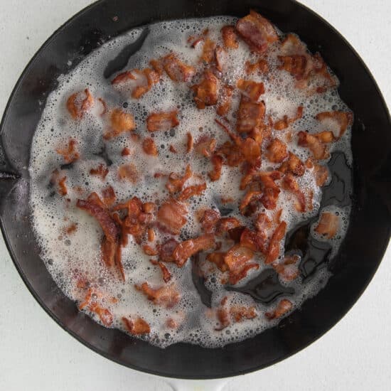 bacon in a frying pan on a white surface.