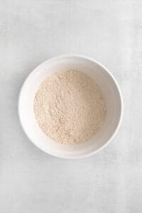 a white bowl of flour on a white surface.