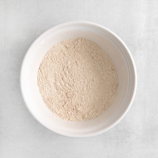 a white bowl of flour on a white surface.