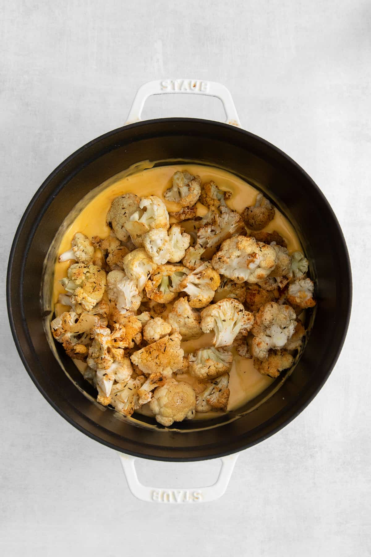 Cauliflower poured over mac and cheese sauce in a bowl.