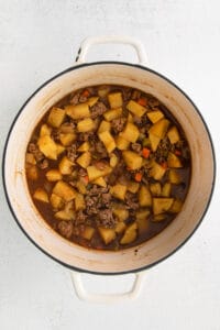 a pot of stew with meat and potatoes on a white background.