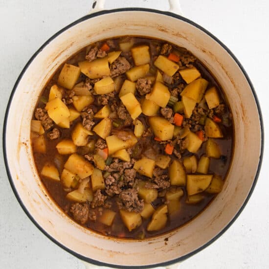 a pot of stew with meat and potatoes on a white background.