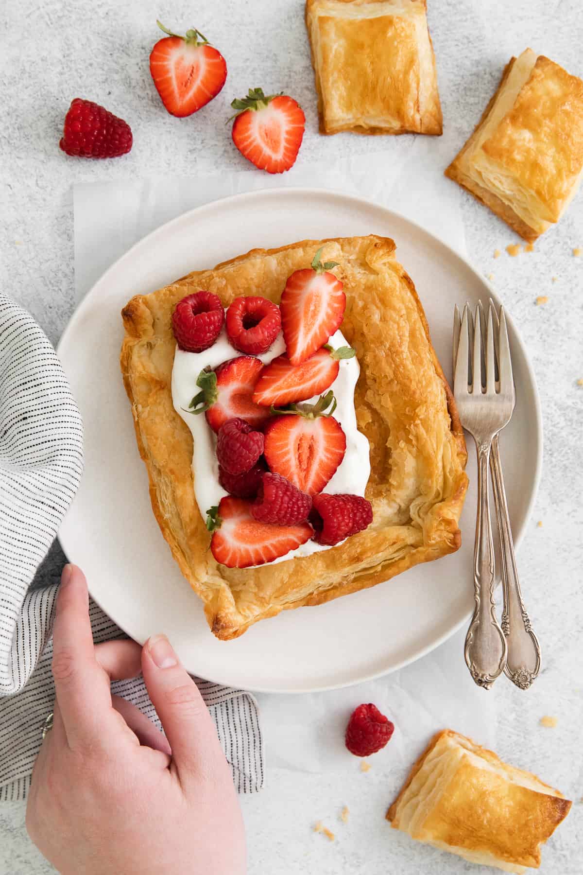 Homemade puff pastry topped with whipped cream and berries on a plate.
