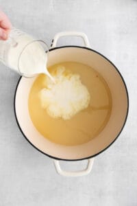 heavy cream being poured into roux and chicken broth mixture