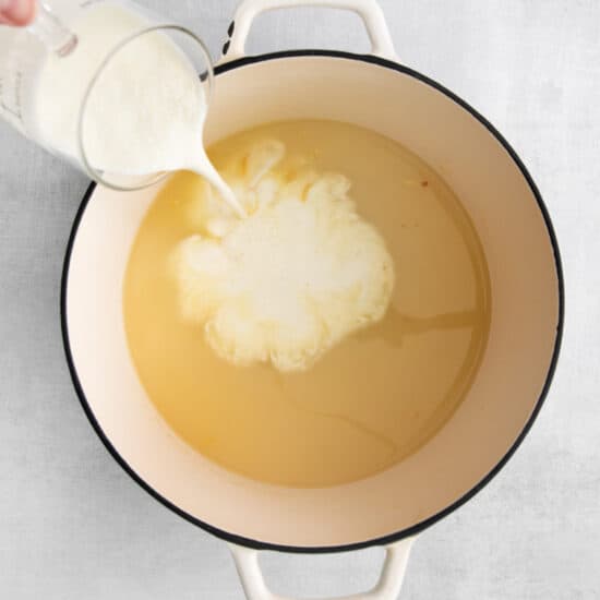 heavy cream being poured into roux and chicken broth mixture