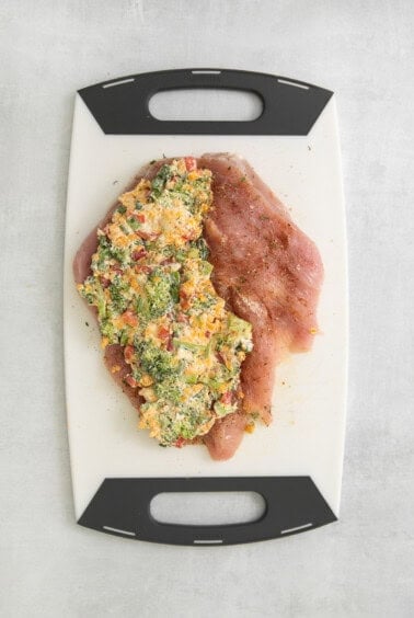 a cutting board with chicken and broccoli on it.