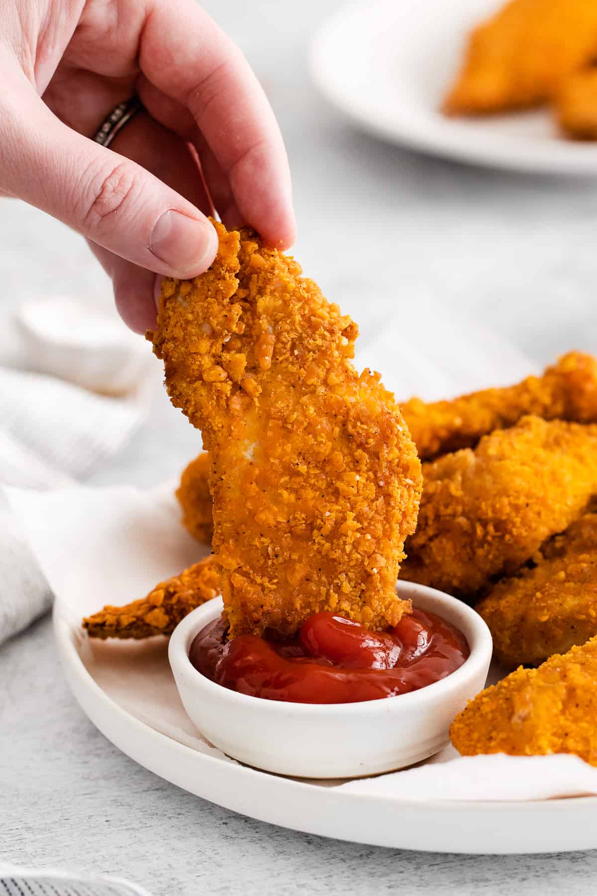 Hand dipping a chicken finger in ketchup.