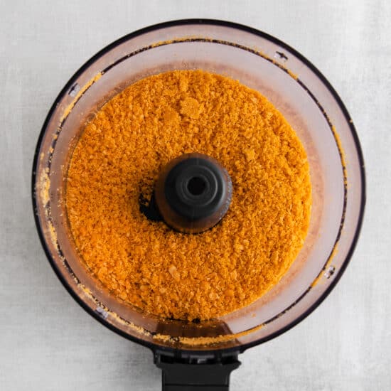 orange powder in a food processor on a white background.