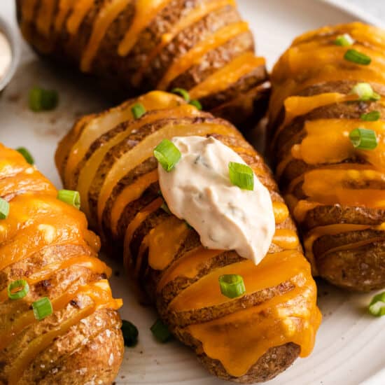 Cheesy hasselback potatoes topped with sour cream and green onions on a plate.