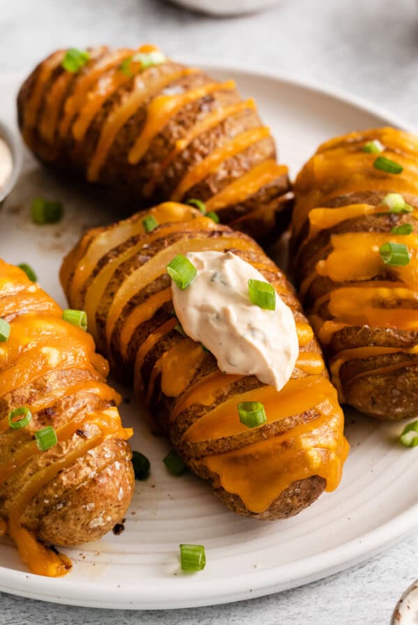 Cheesy hasselback potatoes topped with sour cream and green onions on a plate.