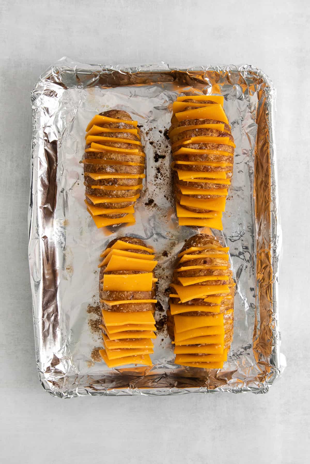 Hasselback potatoes with cheese on a baking sheet.