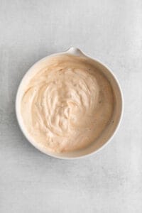 a bowl of creamy sauce on a white surface.