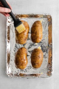 a person using a spatula to brush the potatoes on a baking sheet.