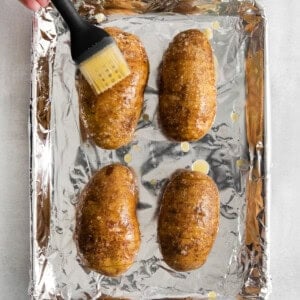 a person using a spatula to brush the potatoes on a baking sheet.