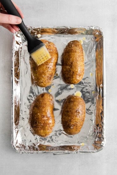 a person using a spatula to brush the potatoes on a baking sheet.