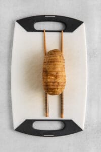 a potato on a cutting board with chopsticks.