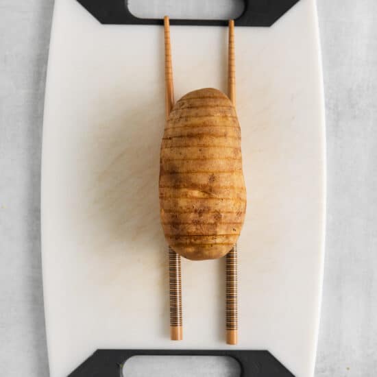 a potato on a cutting board with chopsticks.