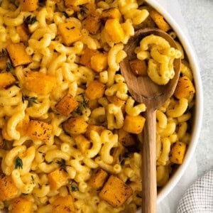 pumpkin macaroni and cheese in a white bowl with a wooden spoon.