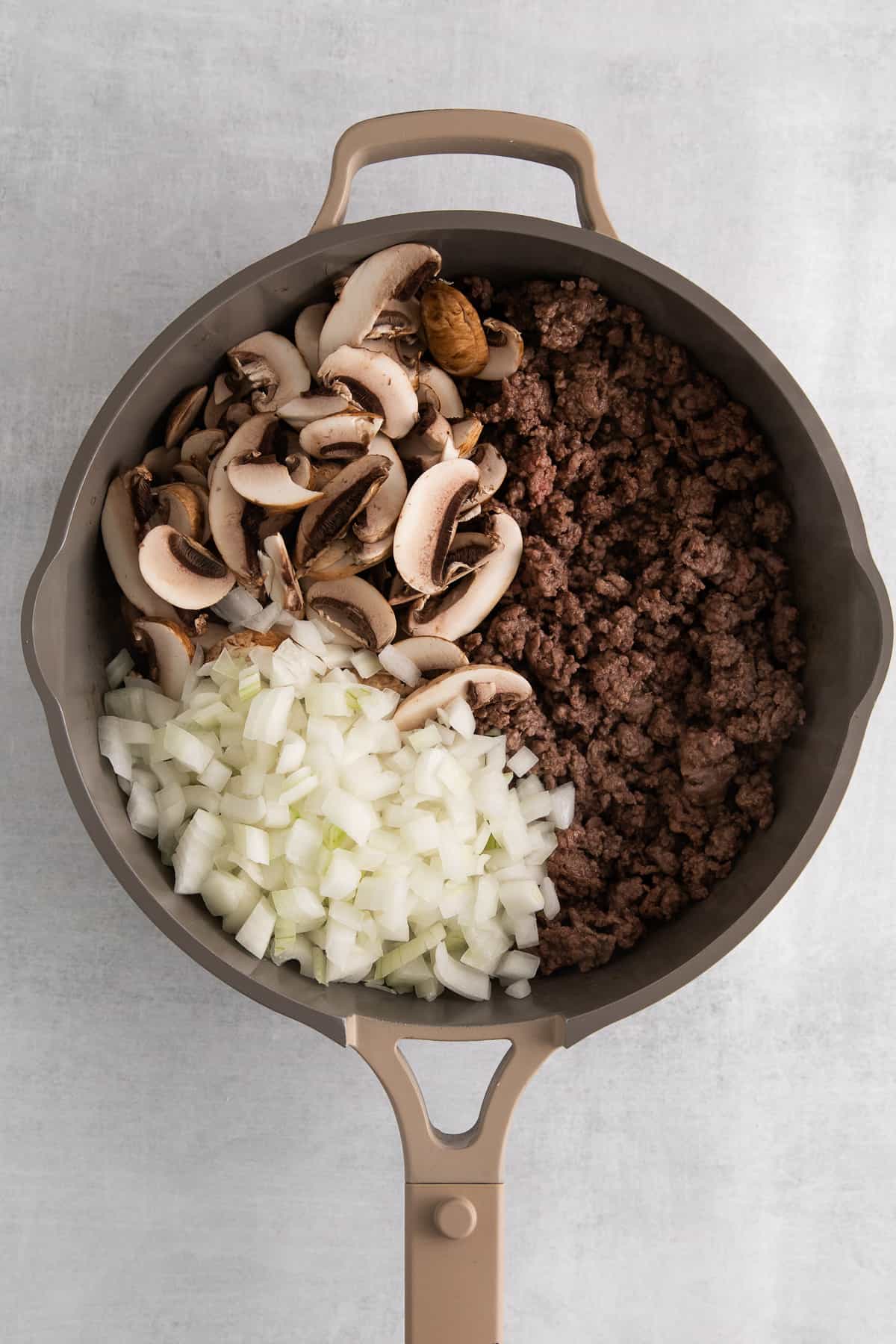 Ground beef, mushrooms and onions in a saute pan.