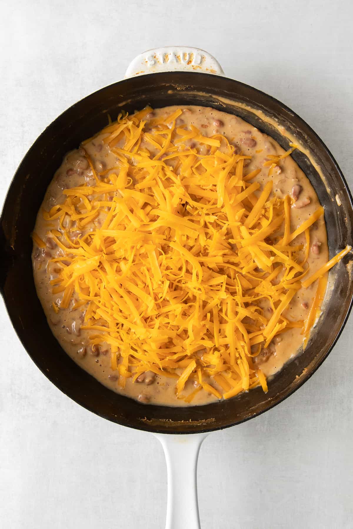 Bean dip topped with shredded cheddar cheese in a cast iron skillet.