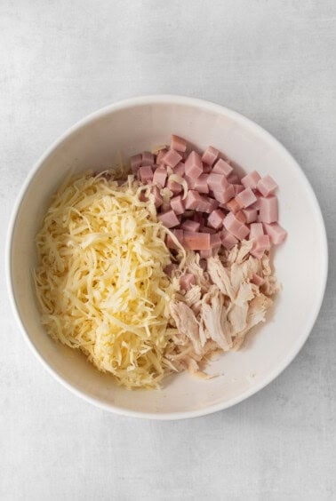 ham and cheese in a bowl on a white surface.