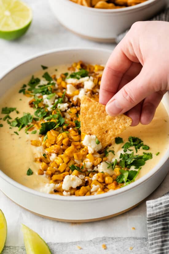 chip dipping into queso in bowl.