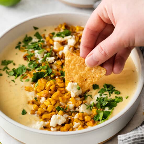a person dipping a tortilla chip into a bowl of corn dip.