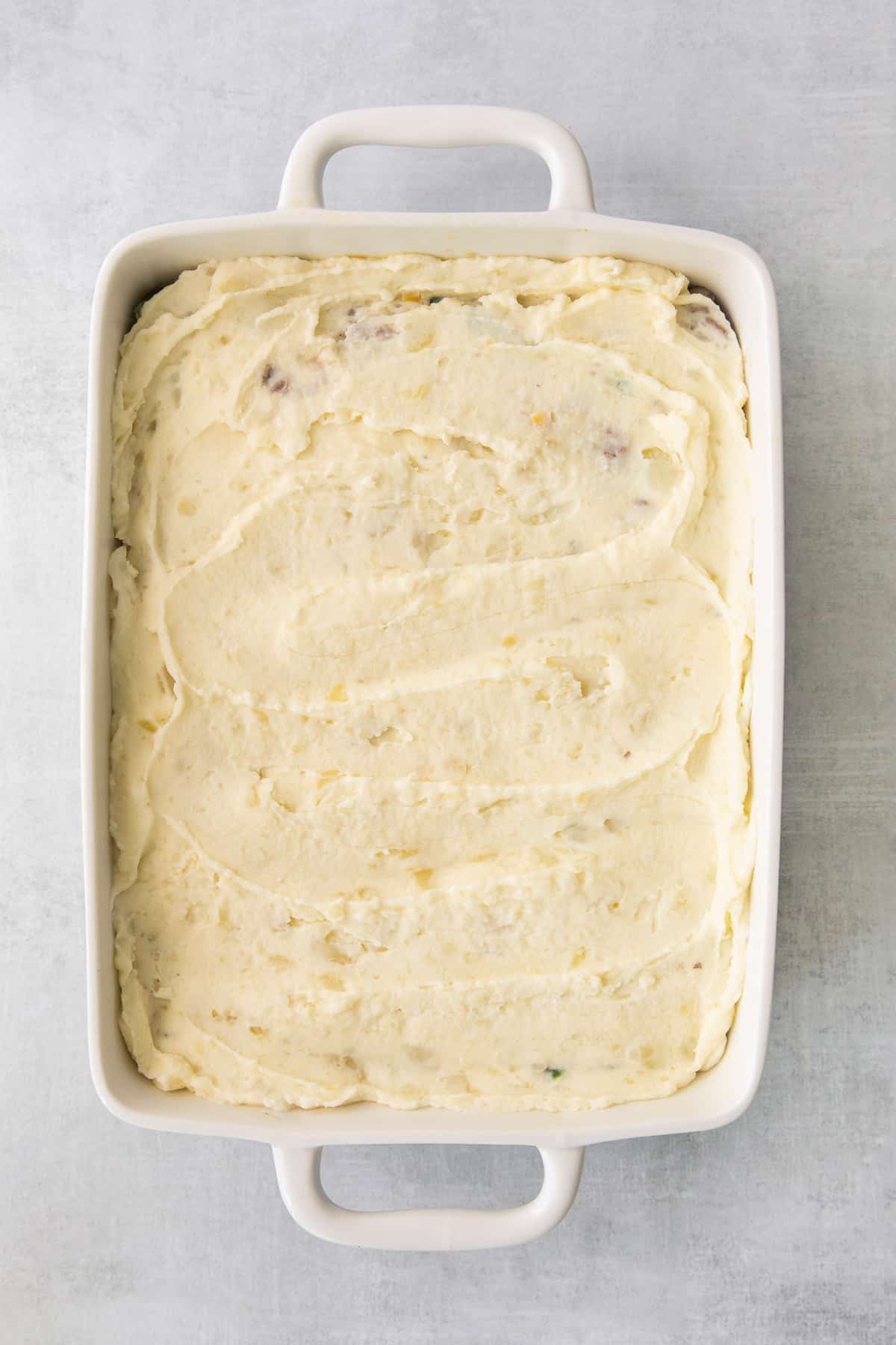 Mashed potatoes on top of shepherd's pie ingredients in a casserole dish.