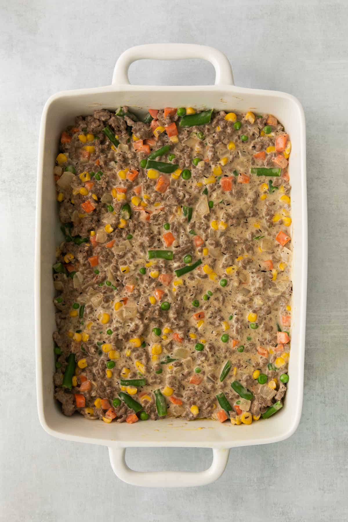 Ground beef and mixed vegetables in a casserole dish.