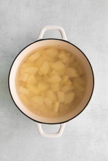 a pot of soup with potatoes in it on a gray background.