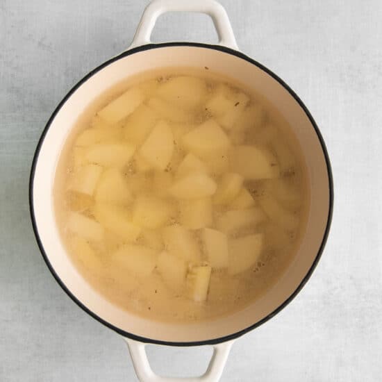 a pot of soup with potatoes in it on a gray background.