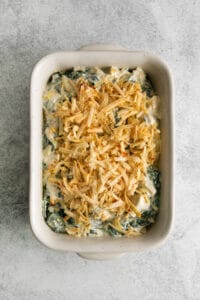 spinach dip in a white dish with shredded cheese on top.
