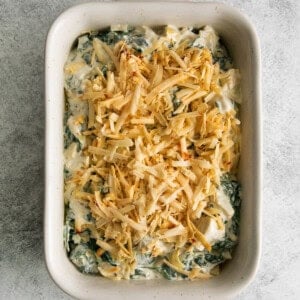 spinach dip in a white dish with shredded cheese on top.