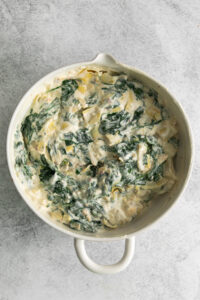 a white dish filled with spinach and cream cheese.