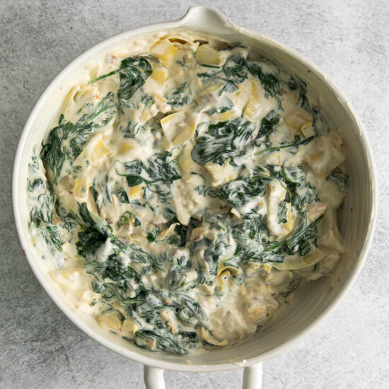 a white dish filled with spinach and cream cheese.