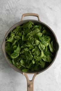 spinach leaves in a frying pan on a gray background.