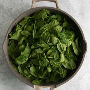 spinach leaves in a frying pan on a gray background.