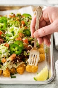 a person holding a fork over a tray of nachos.