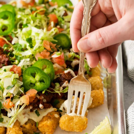 a person holding a fork over a tray of nachos.