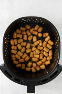a black air fryer filled with tater tots.